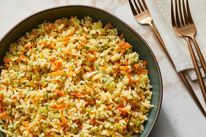 Overhead shot of Baked Rice Pilaf in a large bowl; forks and a napkin are nearby on a marble surface;