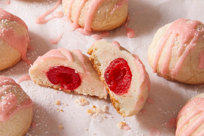 Close-up shot of of Cherry Bonbon Cookies, one sliced open to show the bright red cherry center and soft cookie texture.