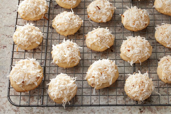 3/4-angle view of Coconut Clouds cookies topped with shredded coconut, lined up on a cooling rack on a speckled countertop;
