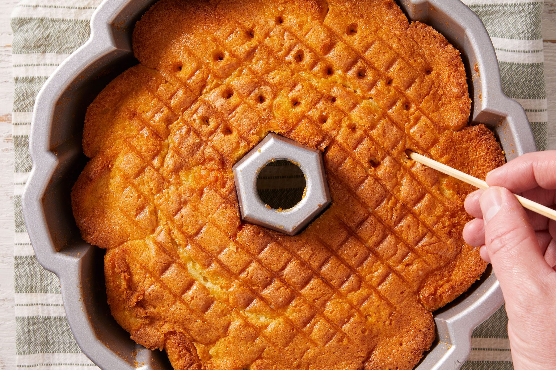 Using a small skewer, poking holes in the coconut rum cake.