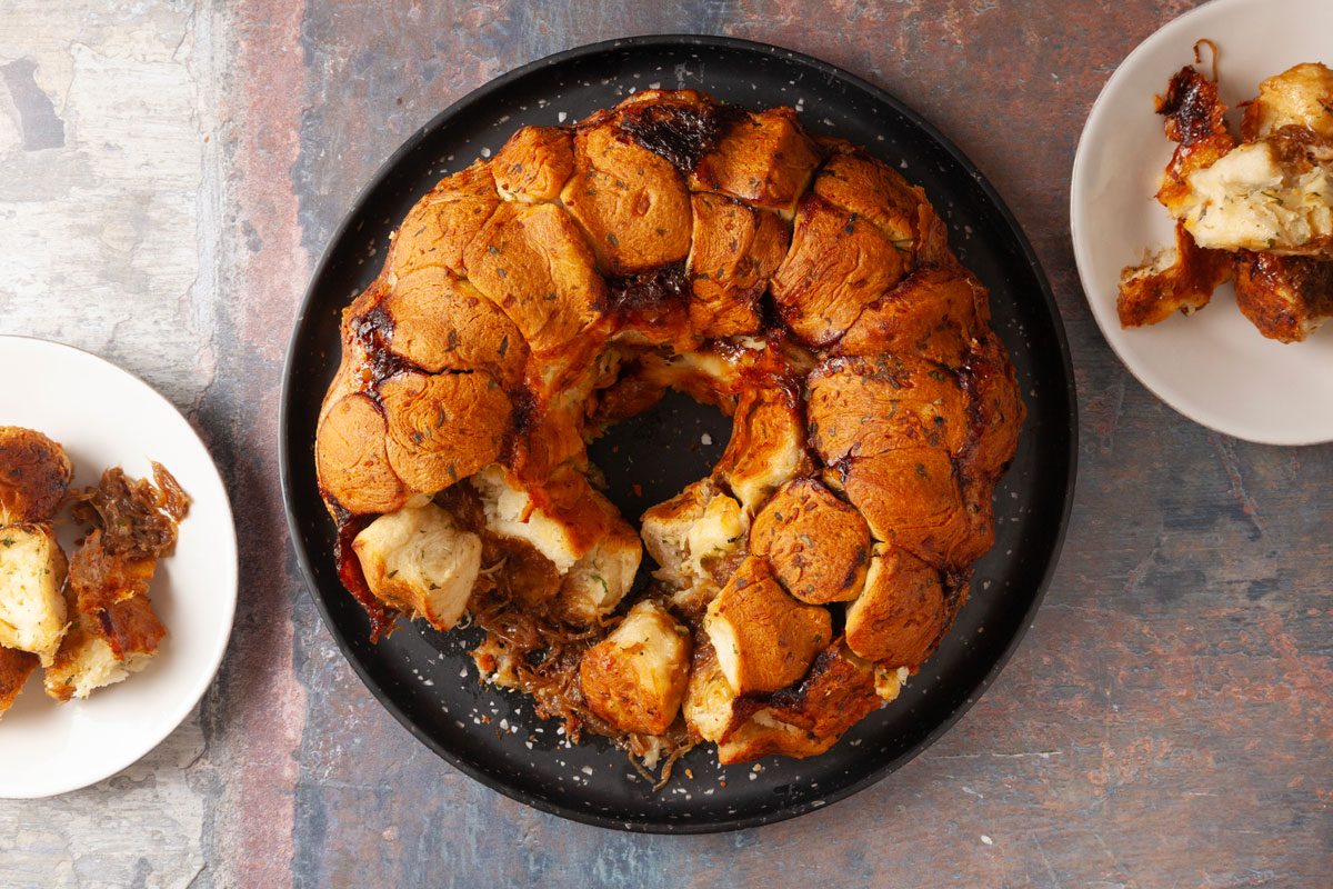Overhead shot of French Onion Monkey Bread, golden-brown and pull-apart, on a black plate, with servings on two smaller plates revealing its soft, layered texture.