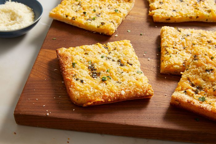 Garlic Cheese Flatbread cut into squares on a wooden board with a dip on side.