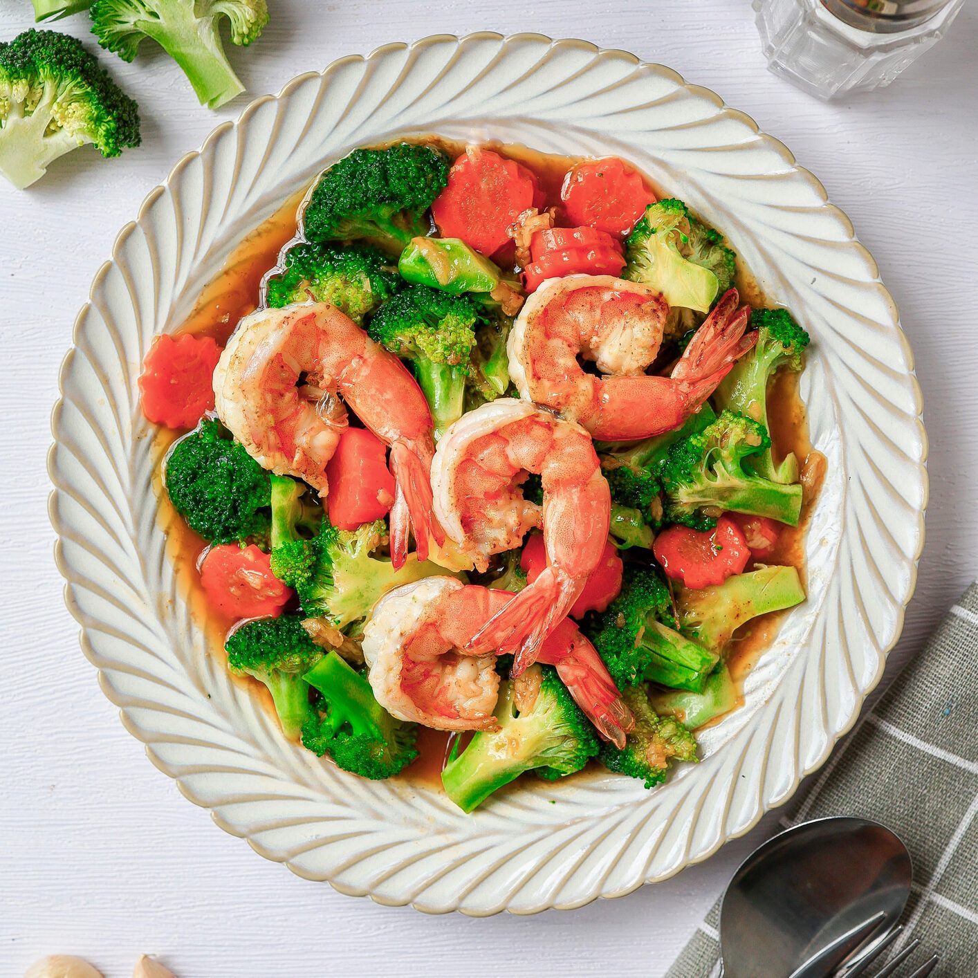 Stir fried broccoli with shrimp in a white ceramic plate witn spoon and fork on white table background
