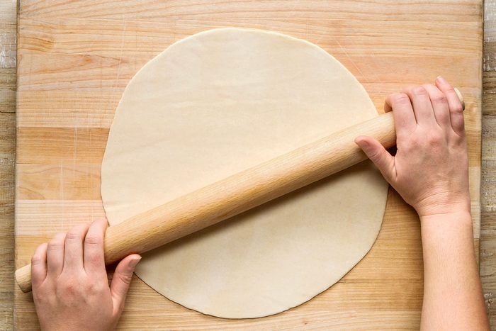 On a lightly floured work surface, rolling a pie dough out into a 12-inch circle using a rolling pin.