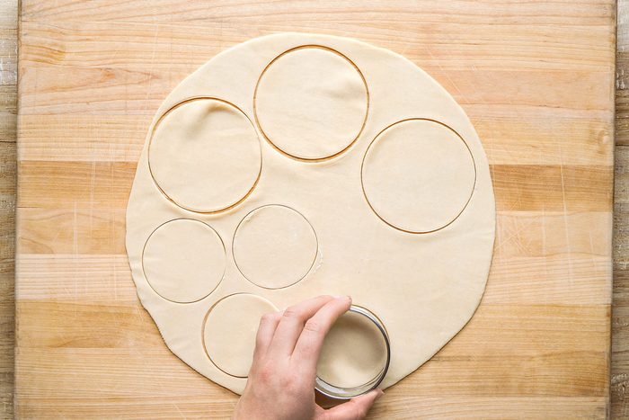 Using floured round cookie cutters, cutthing twenty 4-inch circles and twenty 2-3/4-inch circles on a wooden board.