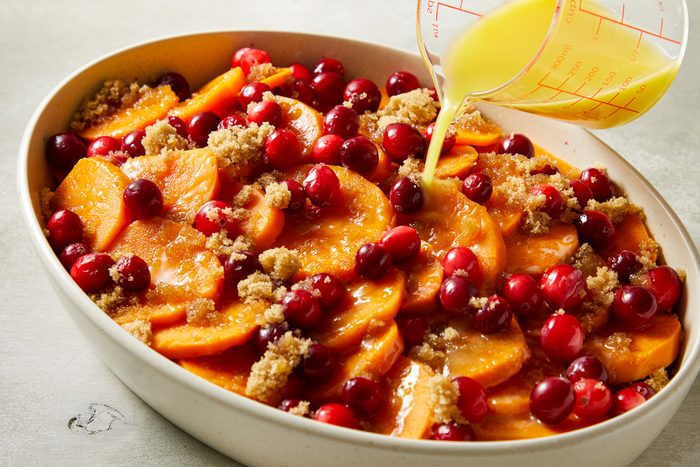 orange juice being poured over potato casserole layers