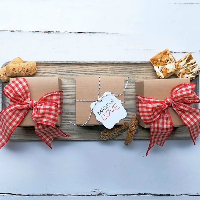Three brown gift boxes on a wooden tray, two tied with red checkered bows and one with twine and a tag reading