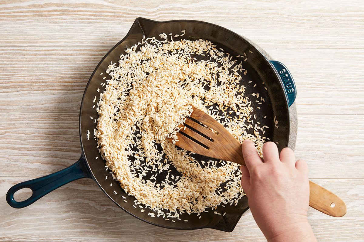 Overhead shot of rice toasting in skillet, stirred by hand.