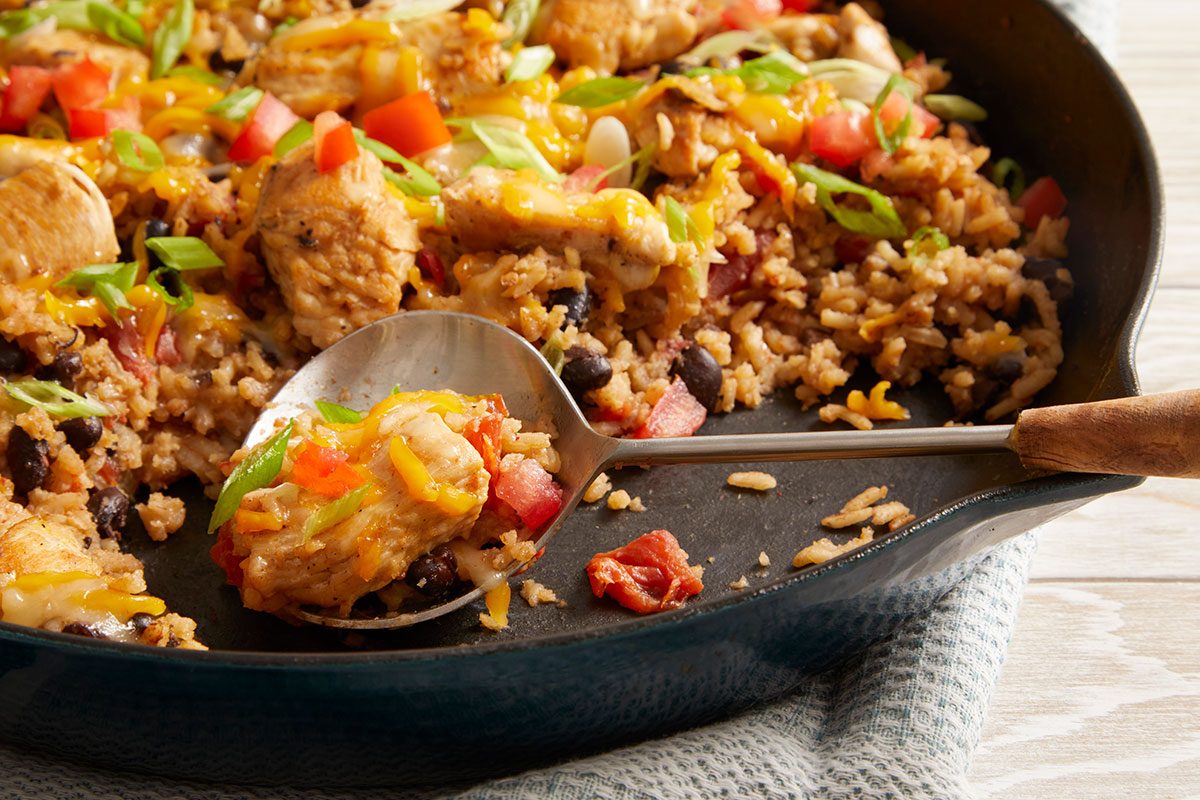 Close up shot of the skillet showcasing Chicken Burrito Skillet over a blue-and-white striped cloth, and a spoon