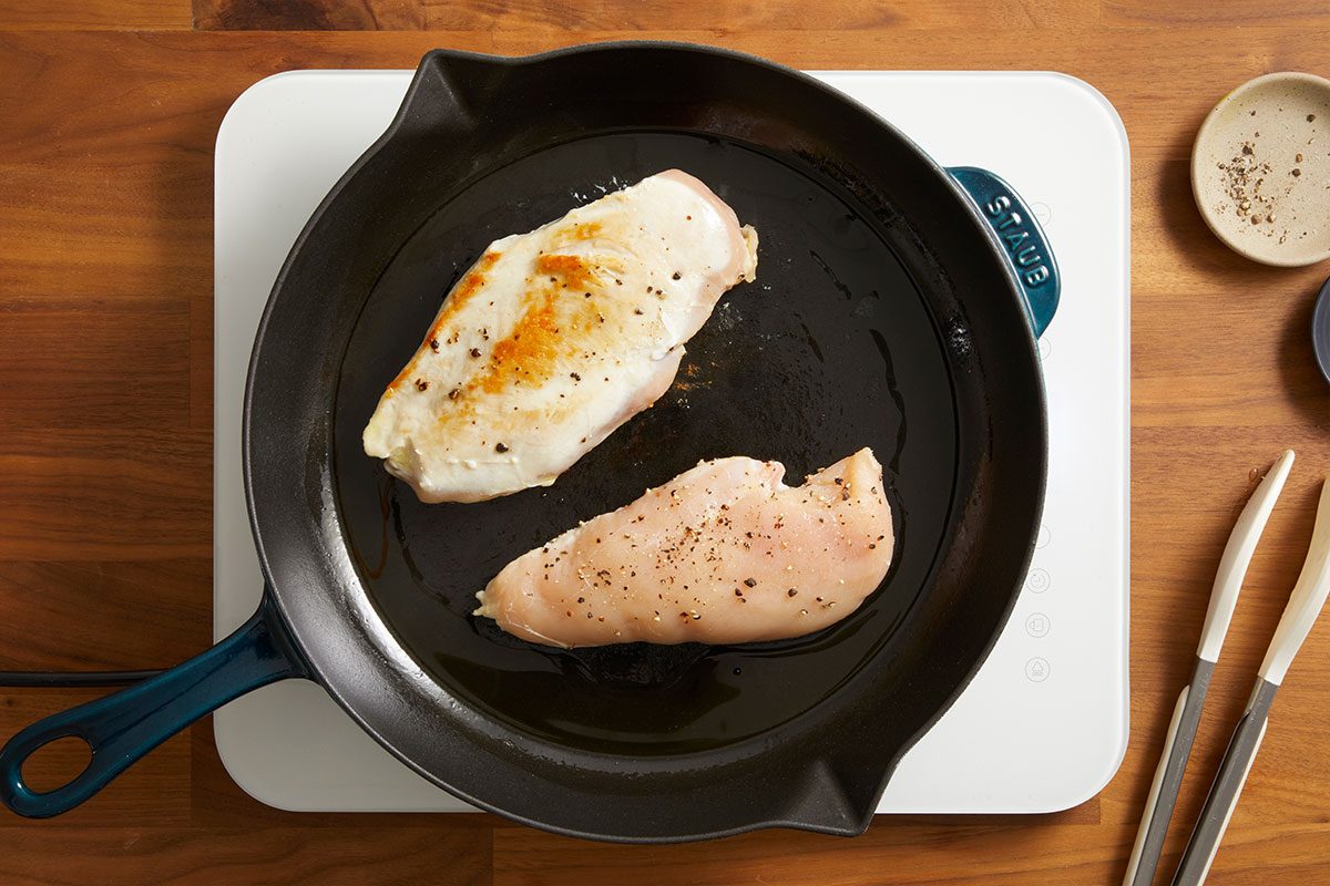 Overhead shot of chicken breasts cooking in a skillet on the stovetop until lightly golden.