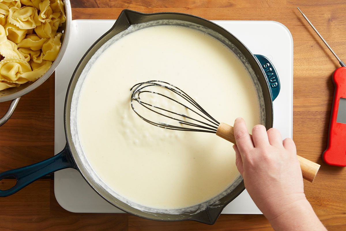 Overhead shot of cheese being whisked into the sauce while pasta is visible nearby, ready to be added.