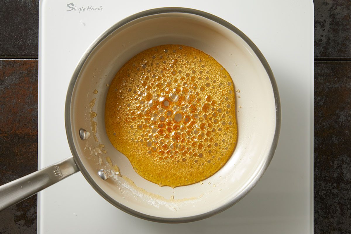 Overhead shot of caramelizing sugar syrup turning golden in a saucepan as it cooks on the stovetop;