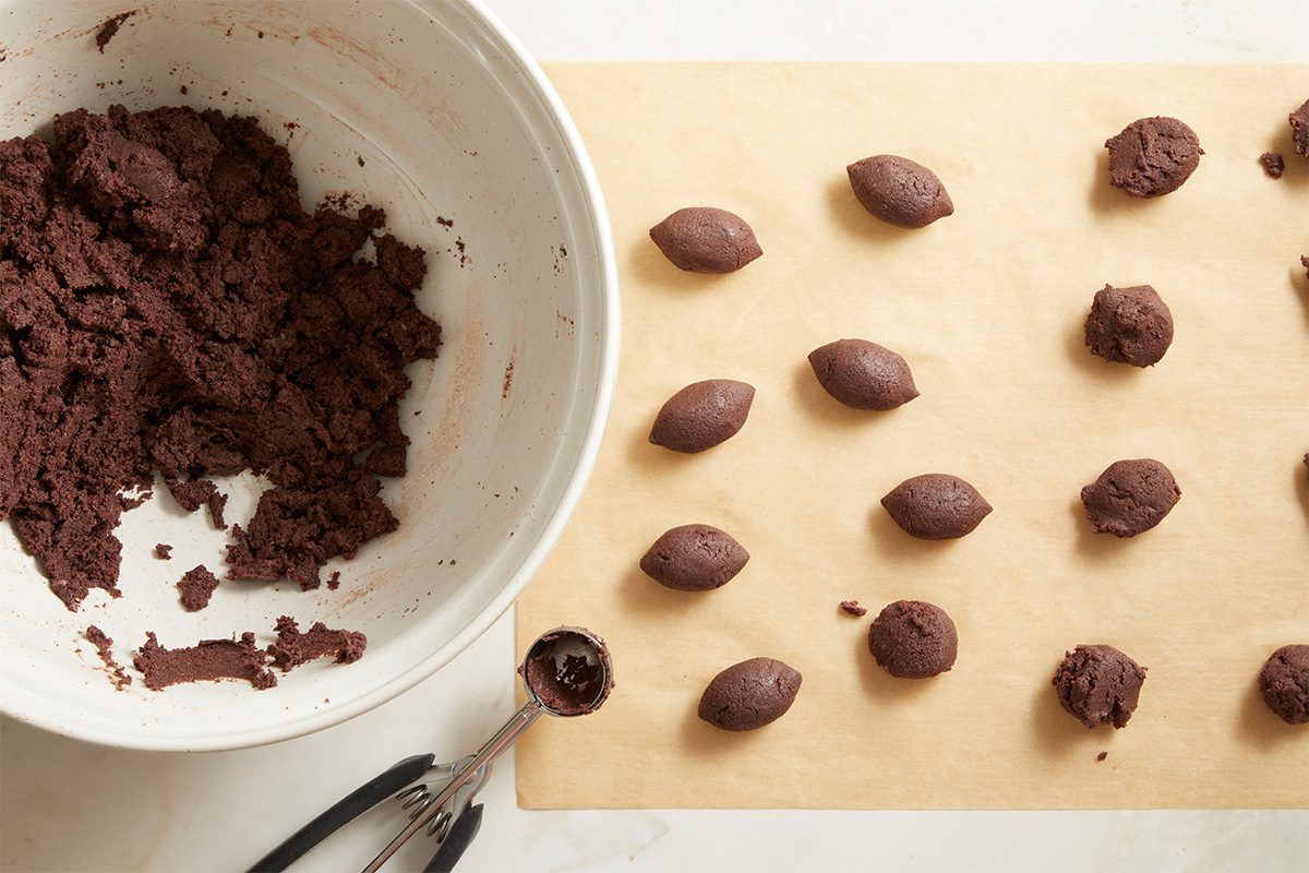 Overhead step-by-step image showing football-shaped cake balls arranged on parchment paper next to a bowl of chocolate cake crumbs during cake pop preparation.