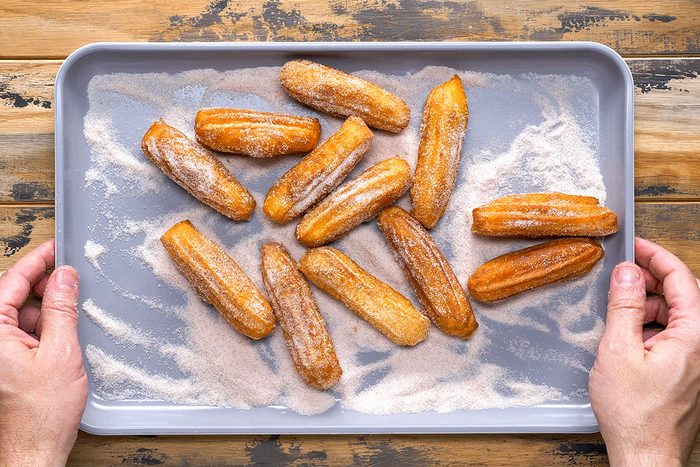 Overhead shot of Homemade churros resting on sugar each one dusted generously the tray sits on a rustic wooden surface