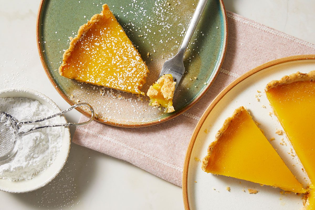 Overhead, horizontal image of a single slice of passion fruit tart plated and dusted with confectioners’ sugar for serving.