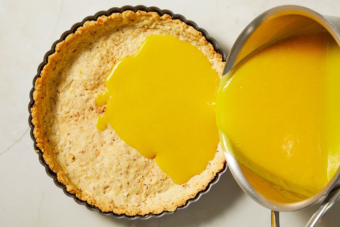 Overhead, horizontal step-by-step image showing passion fruit filling being poured into a prepared almond tart crust before baking.