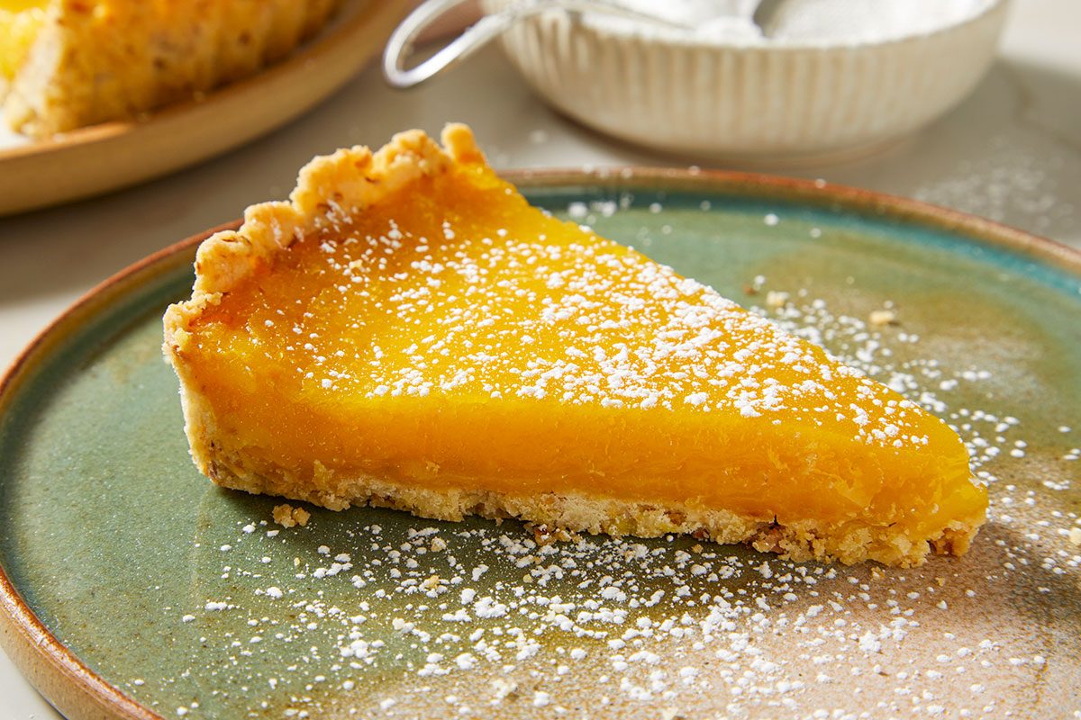 Overhead, horizontal image of a single slice of passion fruit tart plated and dusted with confectioners’ sugar for serving.