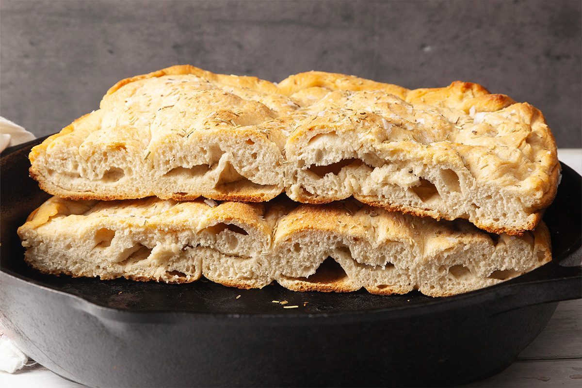 Closeup shot of sliced focaccia stacked inside a cast iron skillet, showing its airy interior texture and golden crust;