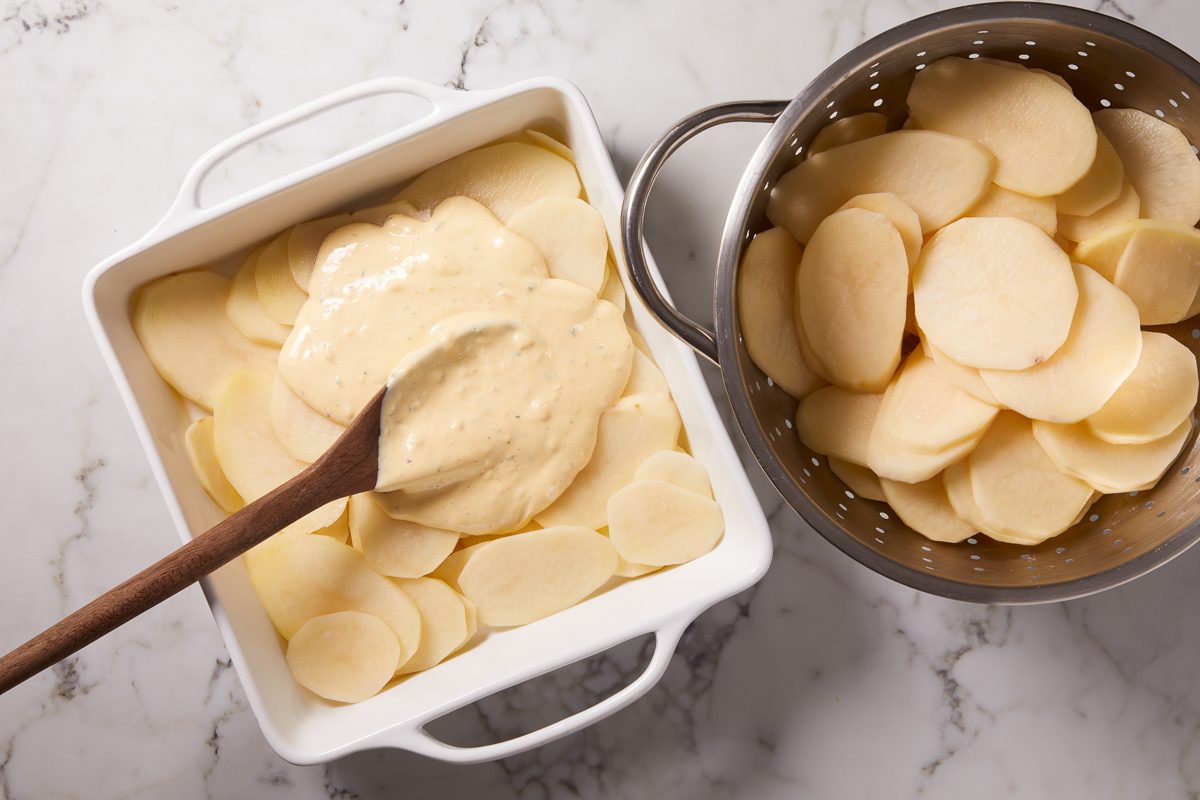 spreading sauce over layer of potatoes in a dish