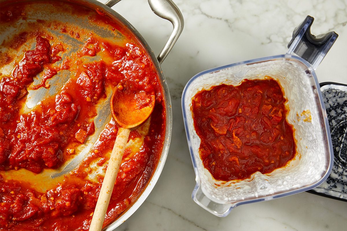 Overhead view of finished tomato vodka sauce in a skillet alongside blended cottage cheese, ready to be combined. The contrast highlights the creamy component that will enrich the sauce.