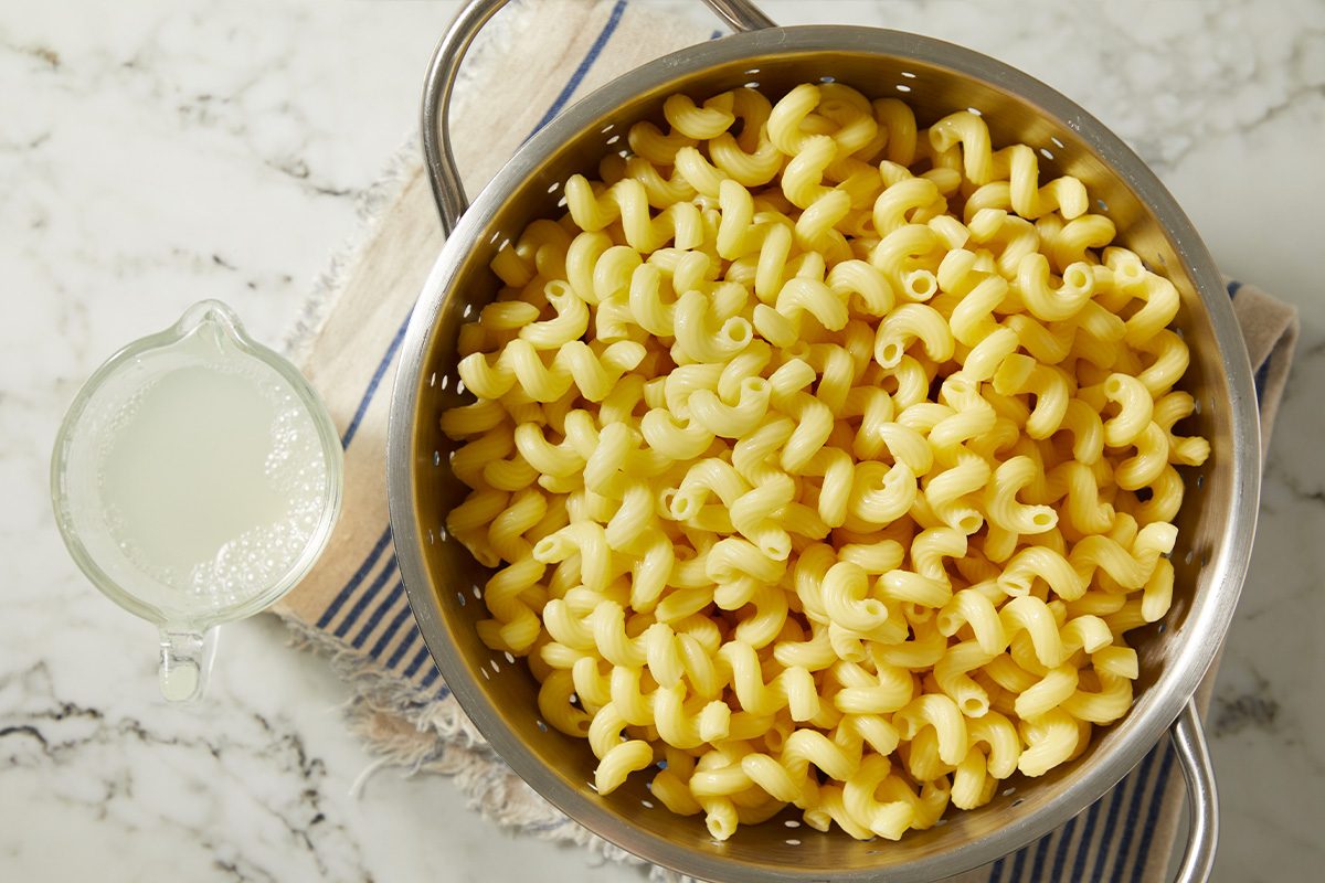 Overhead view of uncooked short-cut pasta boiling in a pot beside the simmering vodka sauce. The pasta cooks to al dente as part of the preparation for a creamy bacon vodka pasta dish.