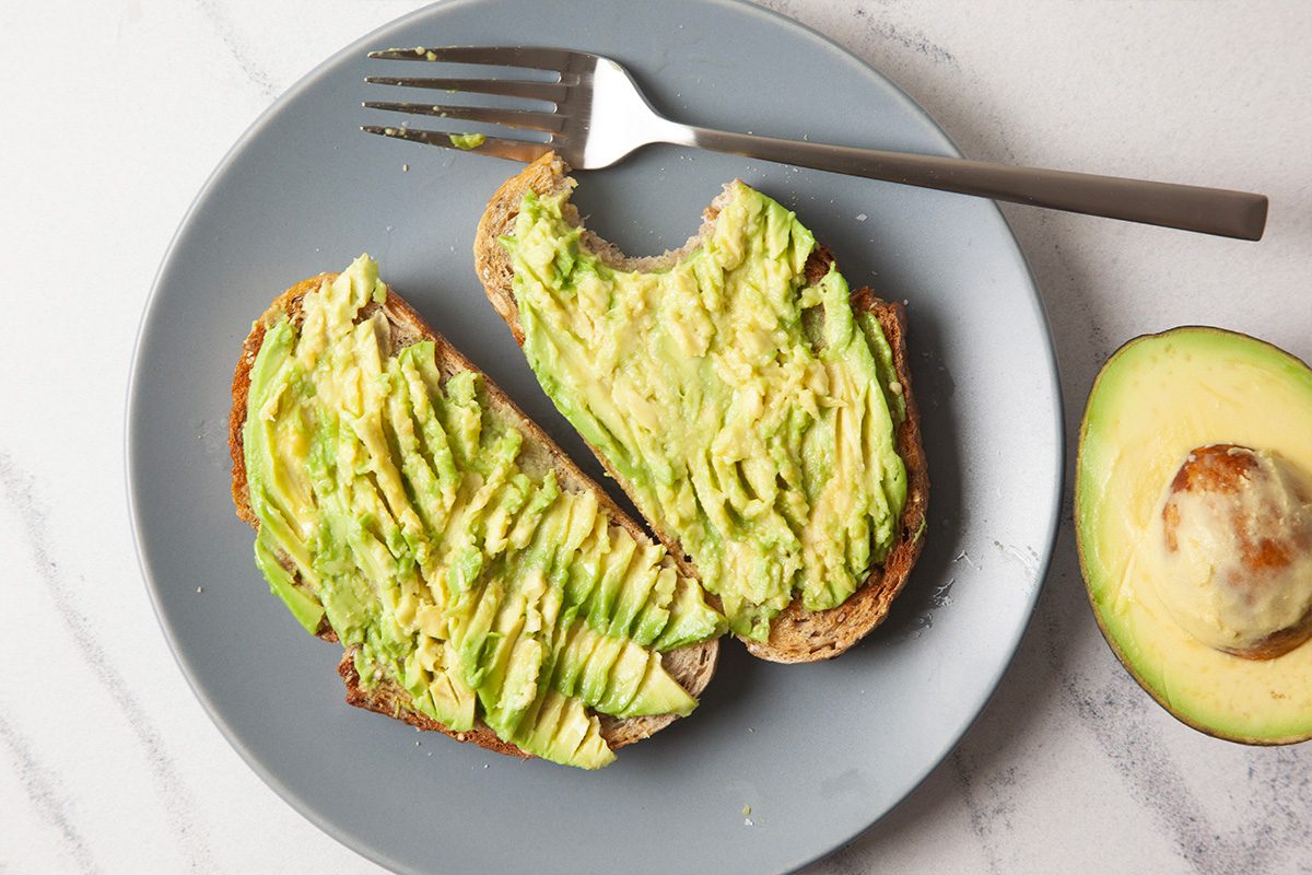 Overhead horizontal image focusing on avocado toast with mashed avocado evenly spread across both slices of toasted bread, highlighting texture and natural color.