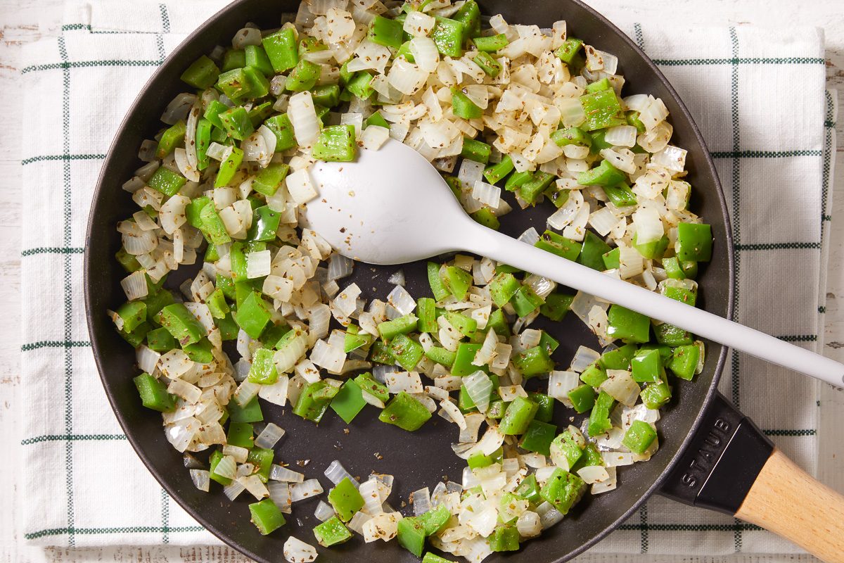 green peppers, onion and topping seasonings being cooked with olive oil in a skillet