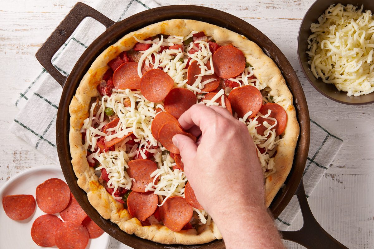 pepperoni being placed on pizza