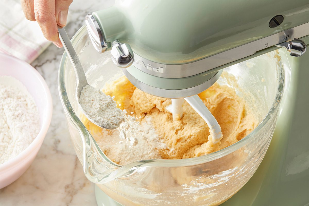 In a small bowl, whisk flour, baking soda and salt; gradually beat into butter mixture. Overhead step-by-step image of cookie dough being blended in a stand mixer. The butter and sugar mixture is being fully incorporated into a smooth batter in preparation for dry ingredients. Clean pastel styling complements the Easter theme.