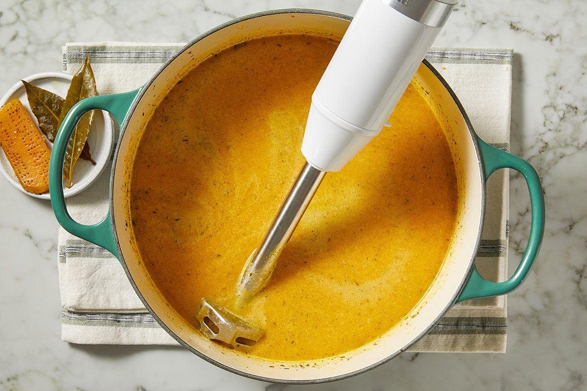 Overhead image of an immersion blender blending soup directly in a Dutch oven, creating a smooth and creamy texture. This step illustrates thickening Italian Penicillin Soup before adding remaining ingredients.