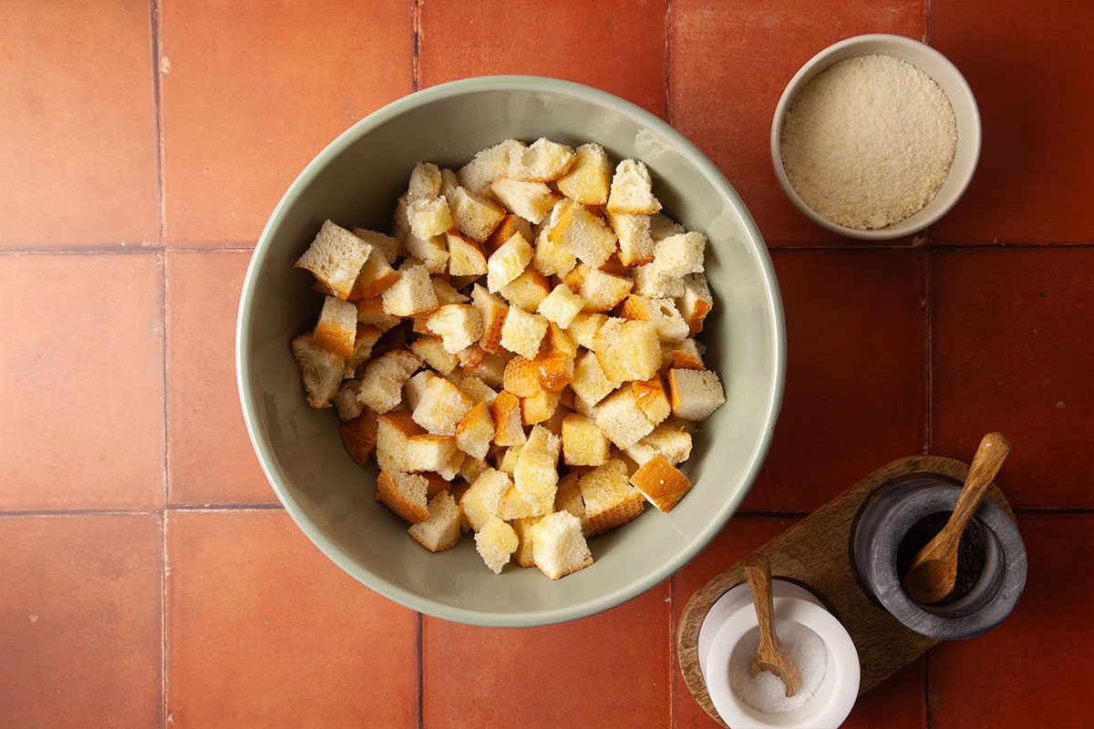 Overhead preparation image showing Italian bread cubes in a mixing bowl ready to be tossed with melted butter, grated Parmesan cheese, salt, and pepper to create crispy, flavorful croutons for Marry Me Chicken Soup.
