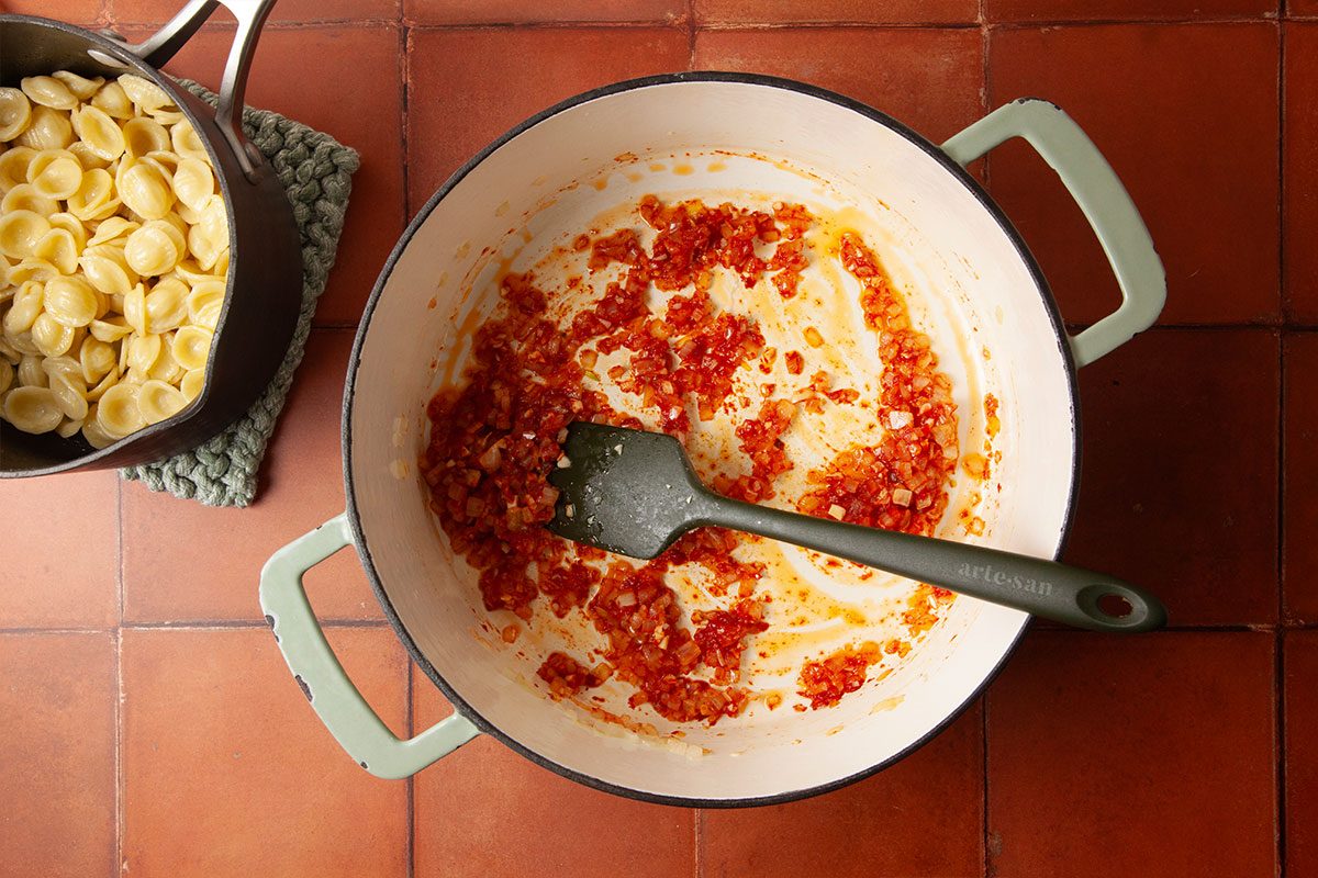 Overhead step-by-step image of tomato paste cooking with onions and garlic in a Dutch oven. A spatula stirs the mixture as the base develops rich flavor for Marry Me Chicken Soup.