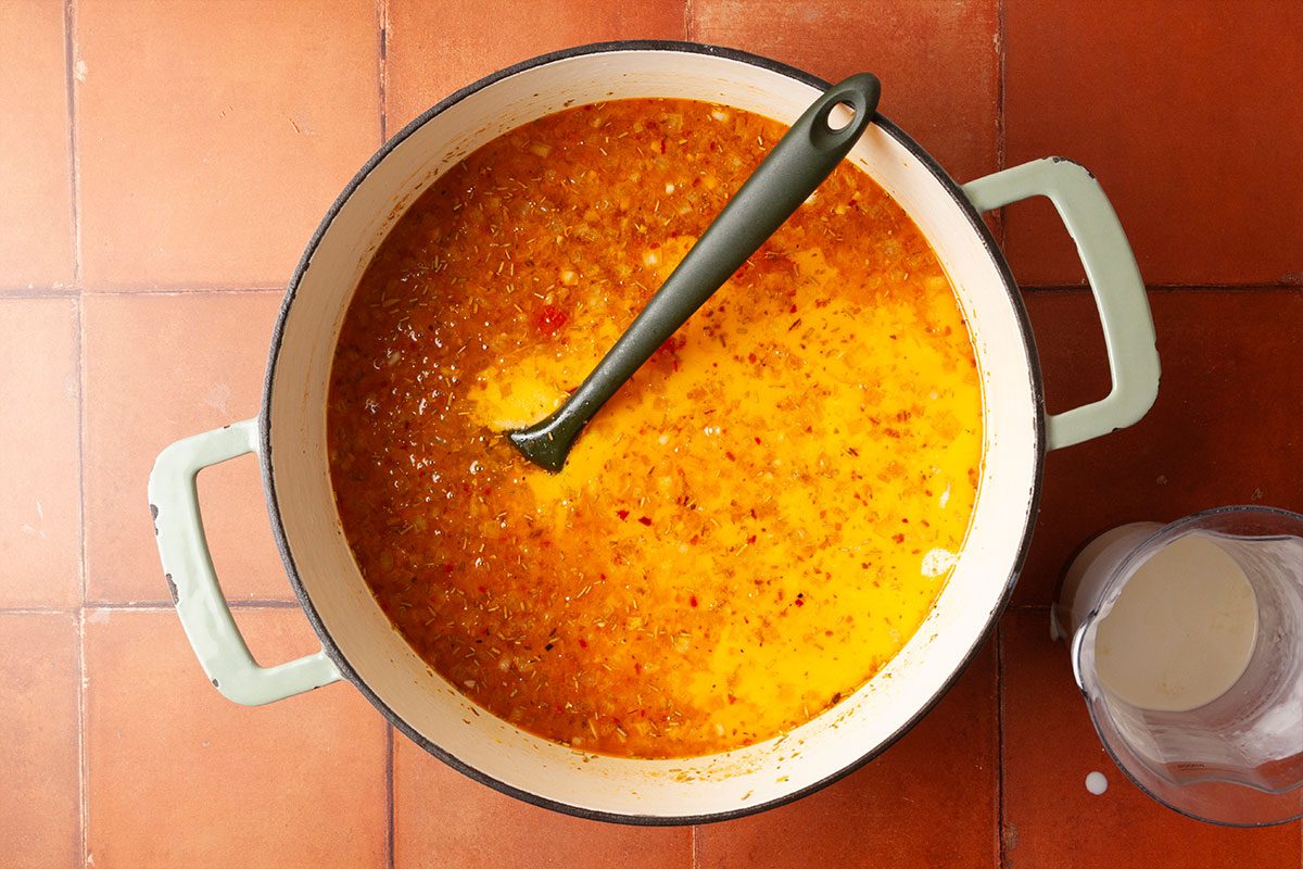 Overhead step-by-step image of heavy whipping cream being added to the simmering tomato broth, creating a creamy, rich base for Marry Me Chicken Soup.