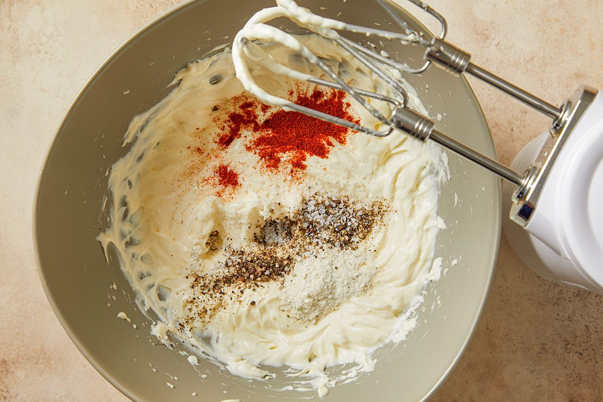 Softened cream cheese blended with mayonnaise and buttermilk in a mixing bowl. Spices including kosher salt, black pepper, cayenne pepper and ranch seasoning are added before mixing.