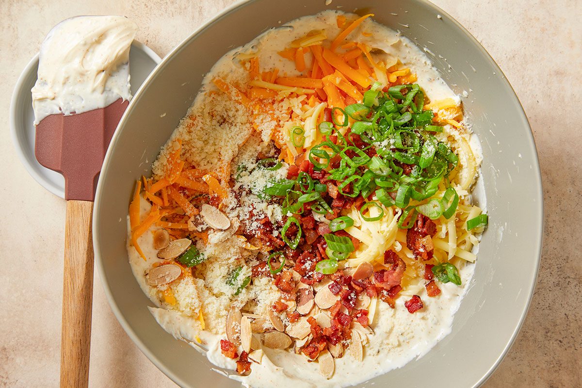 Shredded sharp cheddar, smoked Gouda, grated Parmesan, crumbled bacon, sliced almonds and chopped green onions layered over the cream cheese base before mixing.