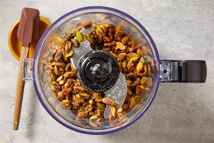 Overhead view of toasted pistachios in a food processor fitted with a blade attachment. The nuts are ready to be blended into a smooth, creamy Pistachio Butter.