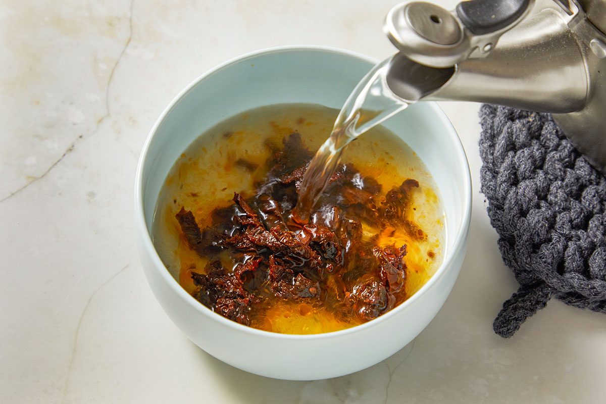 Overhead view of a mixing bowl containing seasonings and liquid ingredients being combined for deviled egg filling. A hand pours oil into the bowl on a light stone surface, showing the initial preparation step for a pull-apart deviled egg Easter carrot recipe.