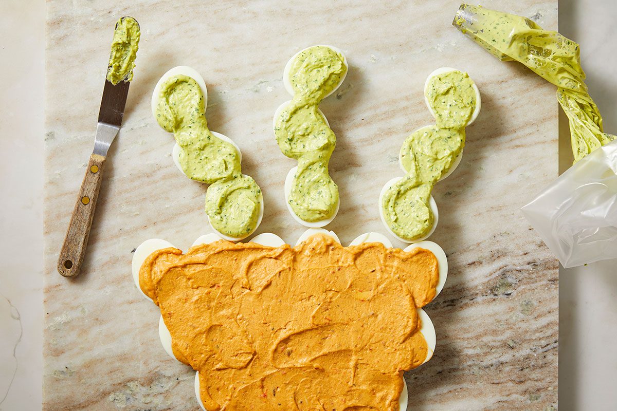 Top-down view of green vegetable slices placed at the top of the carrot-shaped deviled egg arrangement, creating the carrot stem effect.