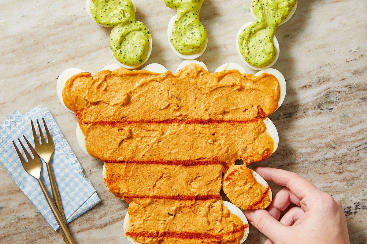 Top-down view of a hand adjusting the deviled egg carrot arrangement before serving, capturing a final styling moment in the recipe process.