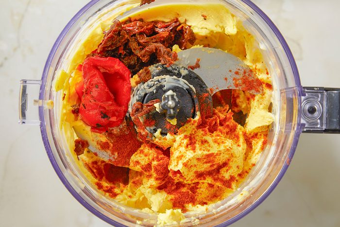 Top-down image of deviled egg filling being blended in a food processor, showing a smooth orange-tinted mixture forming around the blade during processing.