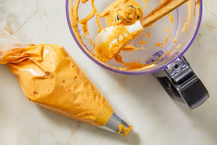 Overhead view of deviled egg filling transferred into a piping bag on a light stone surface, preparing for shaping and assembly of the Easter carrot appetizer.