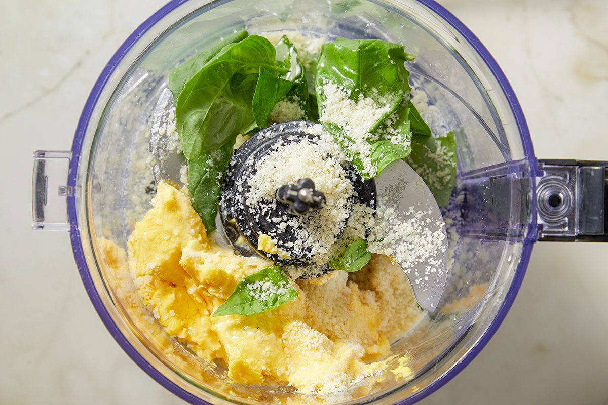 Top-down image showing fresh herbs added to the deviled egg mixture inside a food processor, enhancing flavor and color for the Easter-themed appetizer.