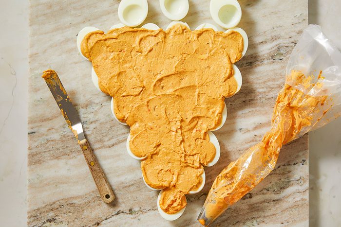 Overhead image of deviled egg filling piped into a triangular carrot shape on a wooden surface, forming the base of the pull-apart Easter appetizer.