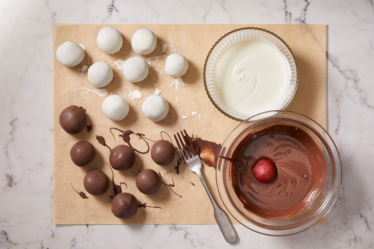 A overhead, horizontal shot of Red Velvet Cake bites on parchement paper having been dipped in a white or black chocolate coating which is then set on parchment paper to dry