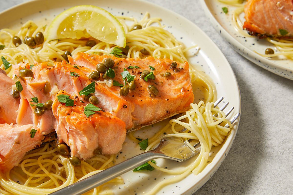 Overhead Push and Pulls image of Salmon Piccata plated with pasta and lemon wedges, showcasing the finished dish ready to serve as a complete meal.