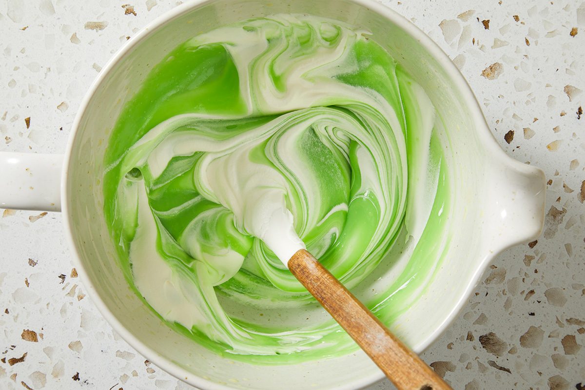Overhead, horizontal step-by-step image showing a fully blended green pie filling swirled smoothly inside a mixing bowl. The creamy texture and uniform color indicate the filling is ready for assembly.