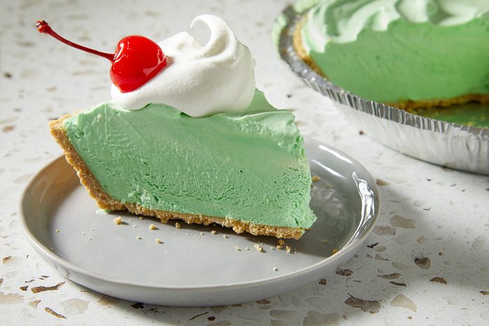 Overhead, horizontal image showing a plated slice of Shamrock Shake Pie with the remaining pie visible in the background. The styled composition highlights serving presentation and portion size.