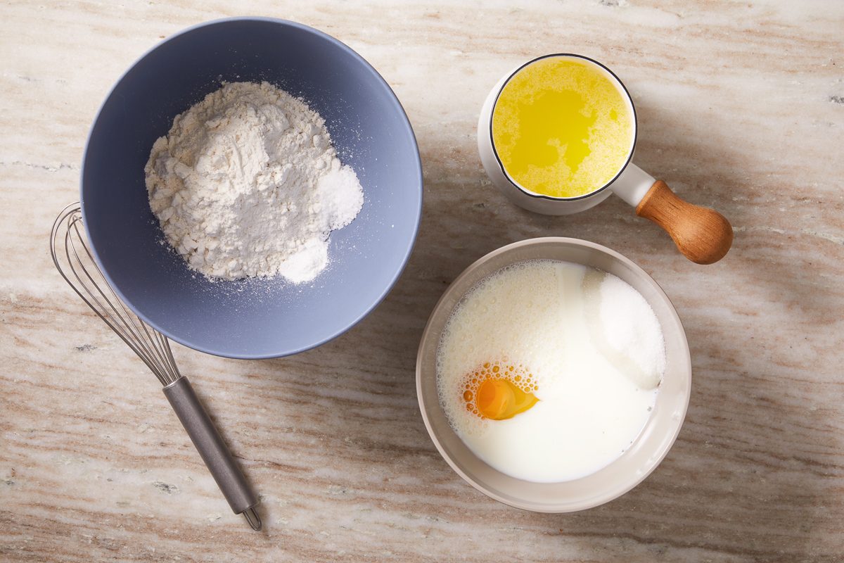 melted butter and bowl with flour, salt and baking powder mixture next to a bowl with eggs, almond extract, milk, sugar and vanilla extract mixture