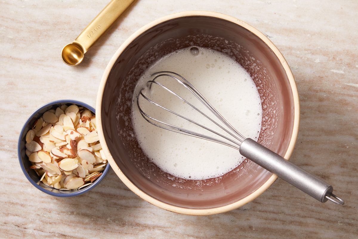 egg whites, almond extract and confectioners' sugar whisked together in a large bowl next to sliced almonds