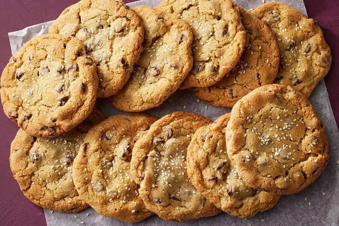 A batch of golden brown chocolate chip cookies with sprinkled sea salt, arranged on a piece of parchment paper.